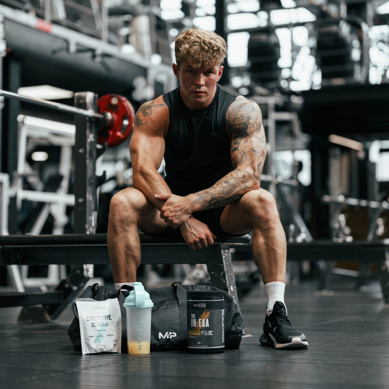 A photo of the coach in a gym sitting on a workout bench with a seriious expression.